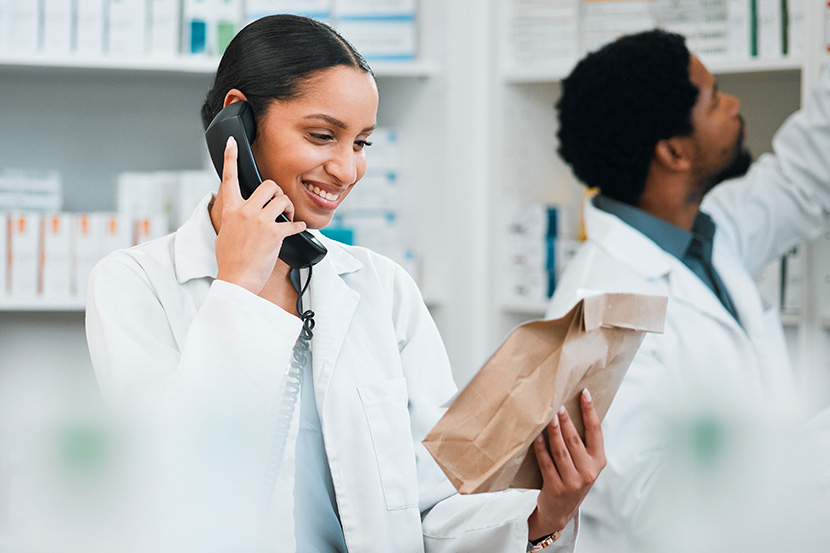Pharmacy student smiling on phone reading a label on a bag.