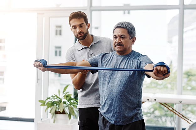physical therapist supporting man stretching bands in gym
